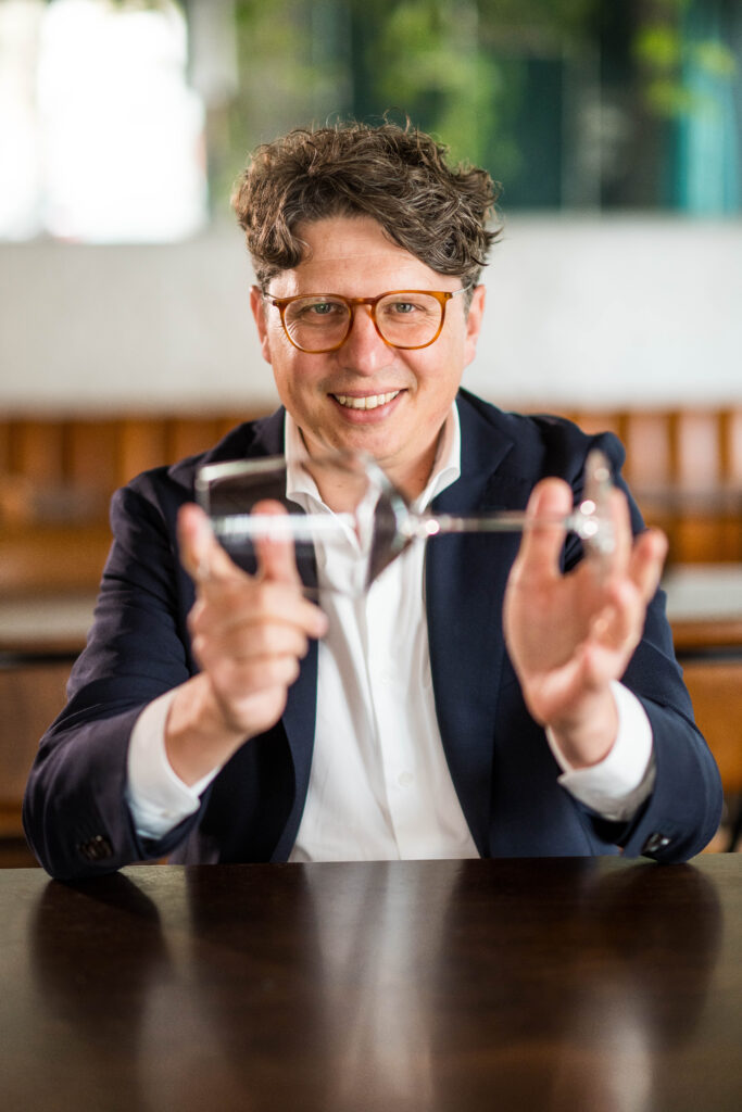 Laurent kijkt spelend naar de camera met een glas wijn